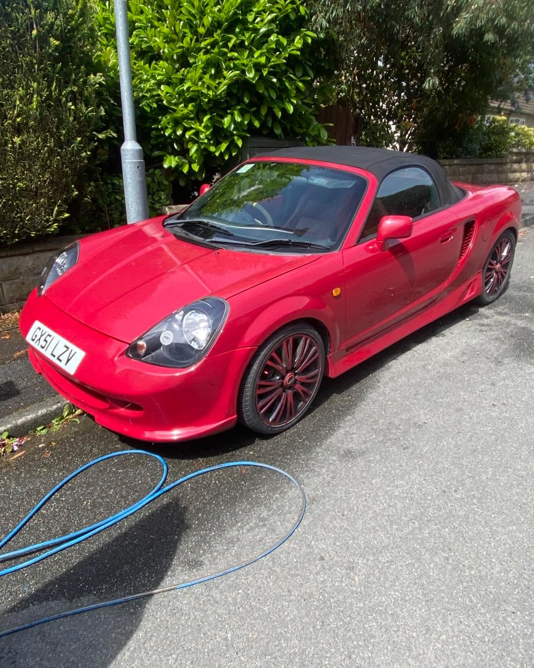 Red coupe mid-wash on the driveway